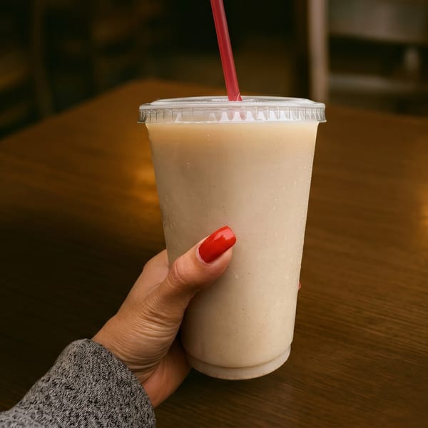 Hand with red nails holding a plastic cup with a light-colored drink and a red straw.