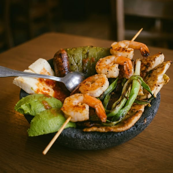 Grilled shrimp skewers, chicken, green peppers, avocado, and cheese in a dark stone bowl.