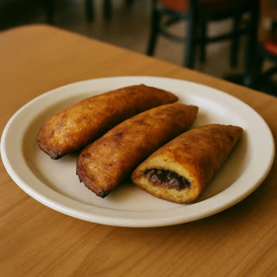 Three golden-brown fried plantains with a dark filling, served on a white oval plate.
