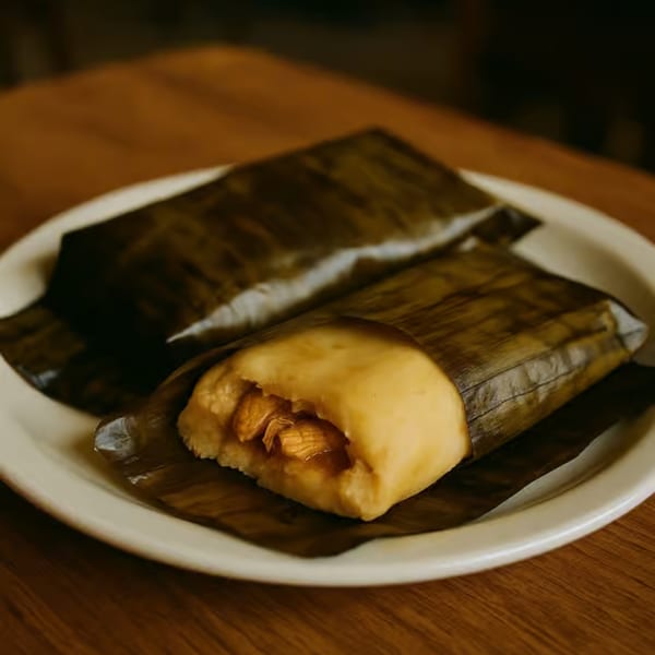 Two tamales wrapped in banana leaves on a white plate, one partially unwrapped to show filling.