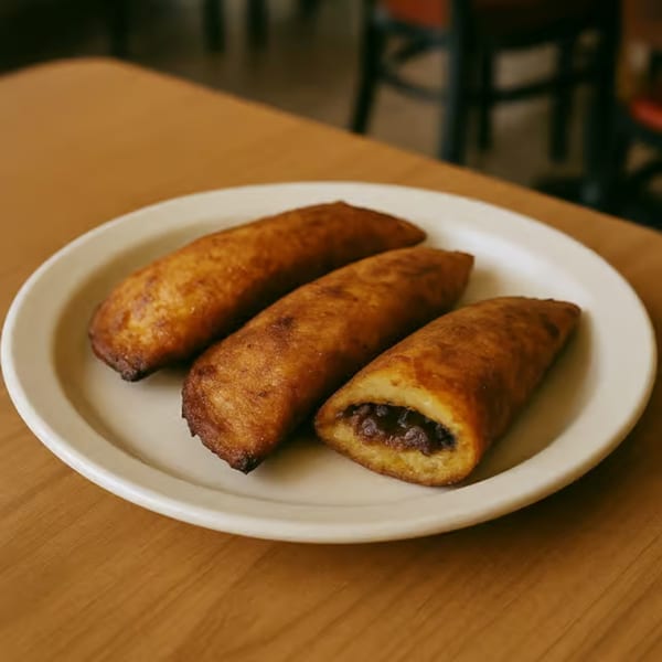 Three golden-brown fried plantains with a dark filling, served on a white oval plate.