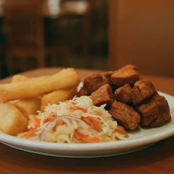 A plate of fried pork chunks, yuca fries, and coleslaw on a wooden table.
