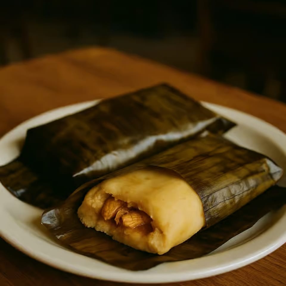 Two tamales wrapped in banana leaves, one partially unwrapped to show the filling.